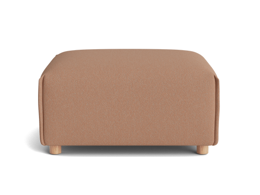 A square, soft ottoman in a warm blush color with light wooden legs, set against a black background.