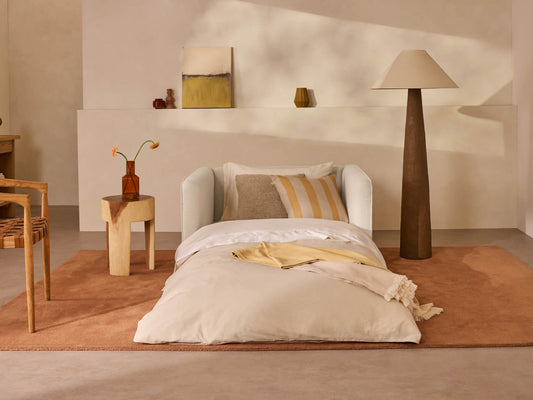 A light beige sofa with striped pillows on a terracotta rug, complemented by a dark brown floor lamp and a wooden side table.