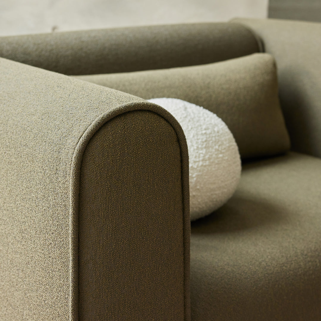 Curved-arm olive green armchair with textured white and matching cushion.