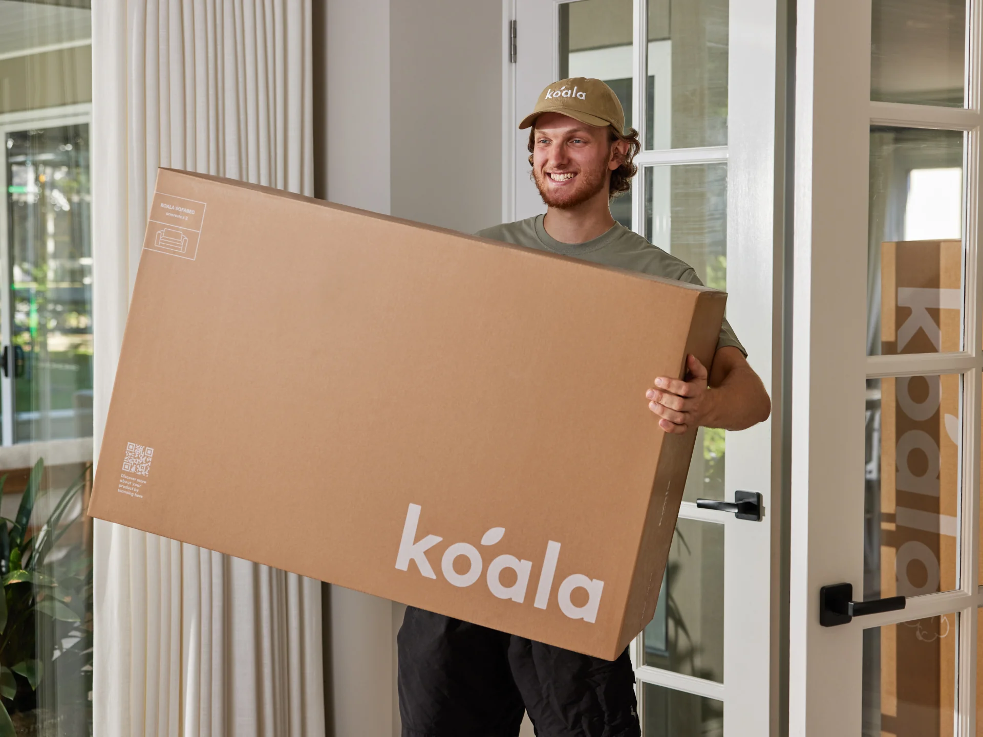 Man holding a large cardboard box with 'koala' branding in a home setting.
