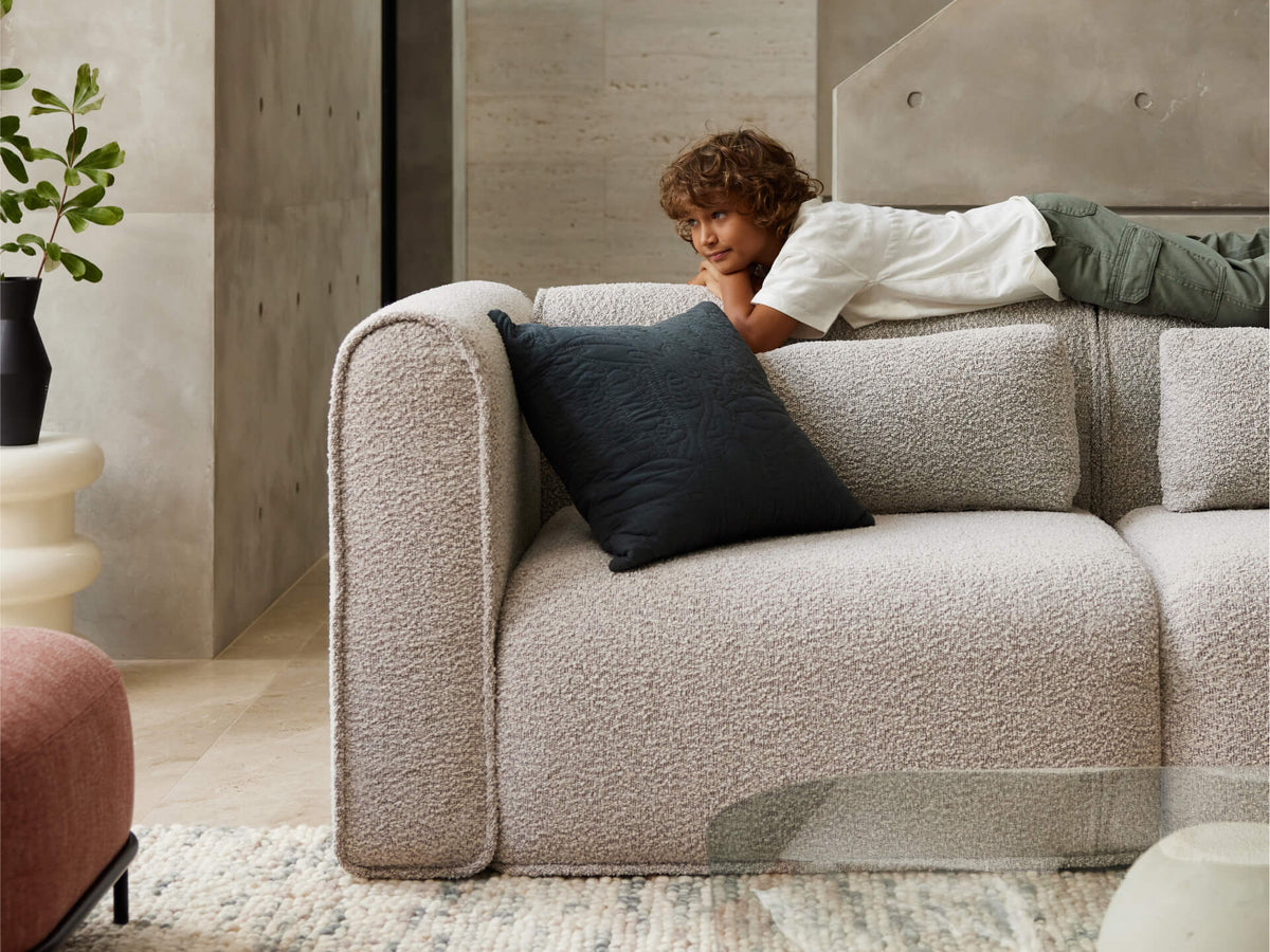 Luxurious grey boucle sofa with plush cushioning, featuring a plush navy accent cushion. Set in a modern, minimalist living room with neutral tones.