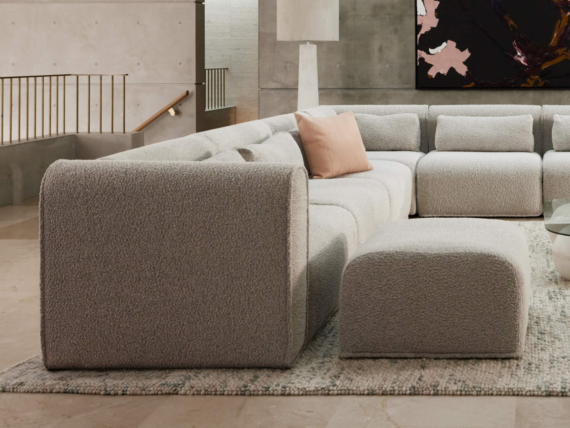 Luxurious grey boucle sectional sofa with plush cushions, complemented by an ottoman. Set in a modern, minimalist living area with a neutral palette.