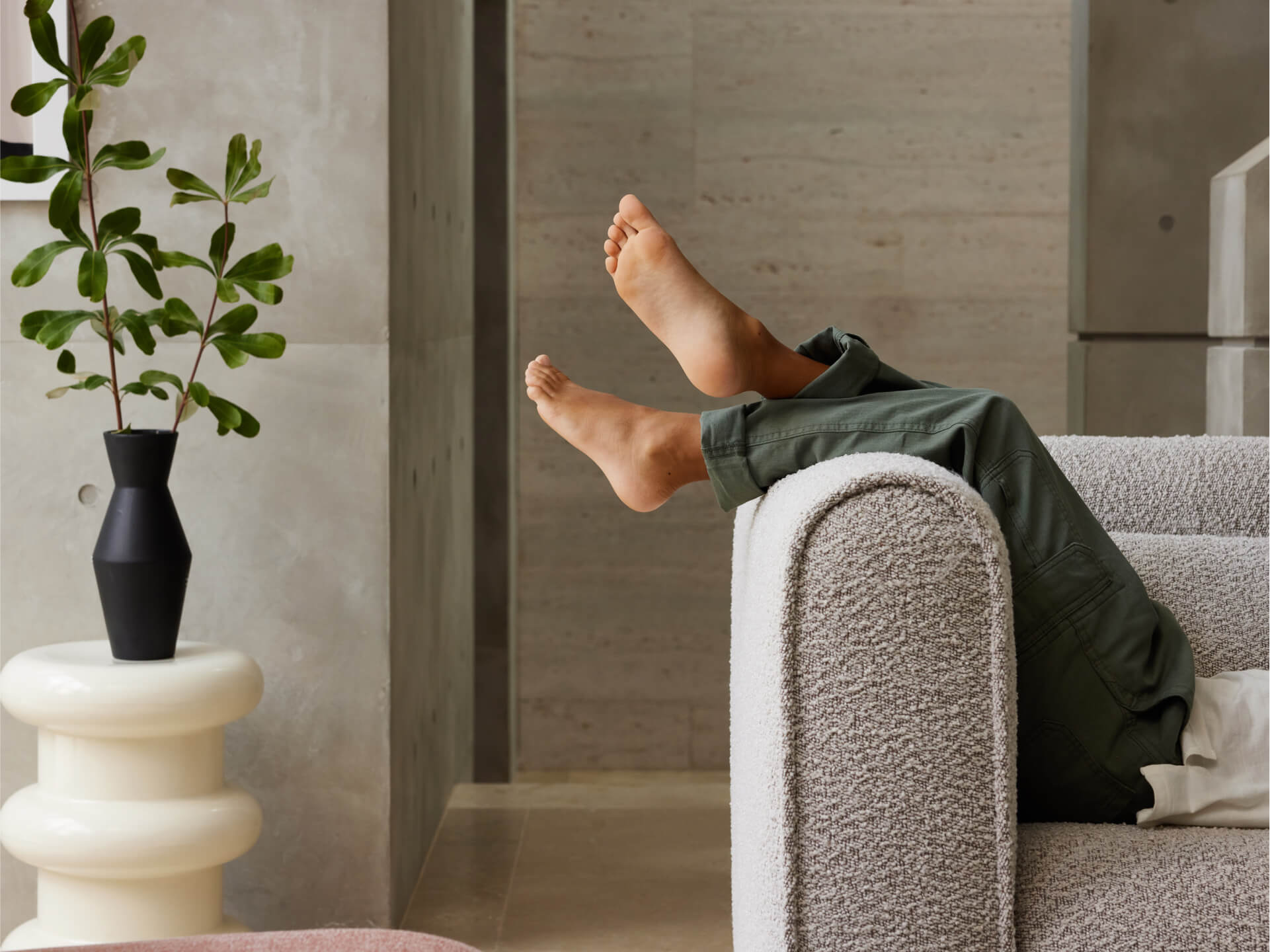 Plush boucle sofa in light grey, featuring a rounded armrest design, blends seamlessly into a modern interior with textured concrete walls.