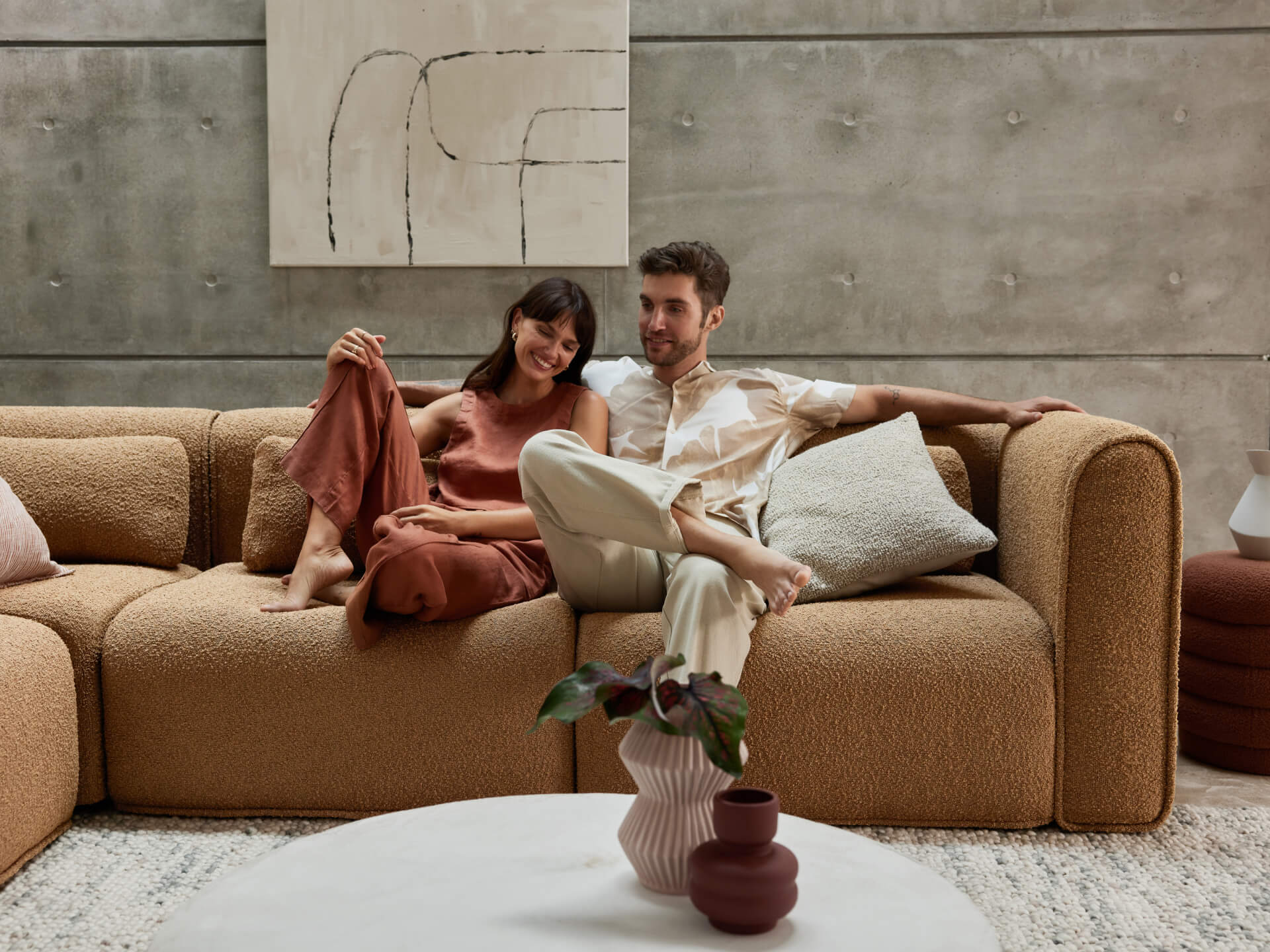 Plush boucle sectional sofa in warm beige with modular design, set against a textured concrete wall. Complements a minimalist, contemporary living space.
