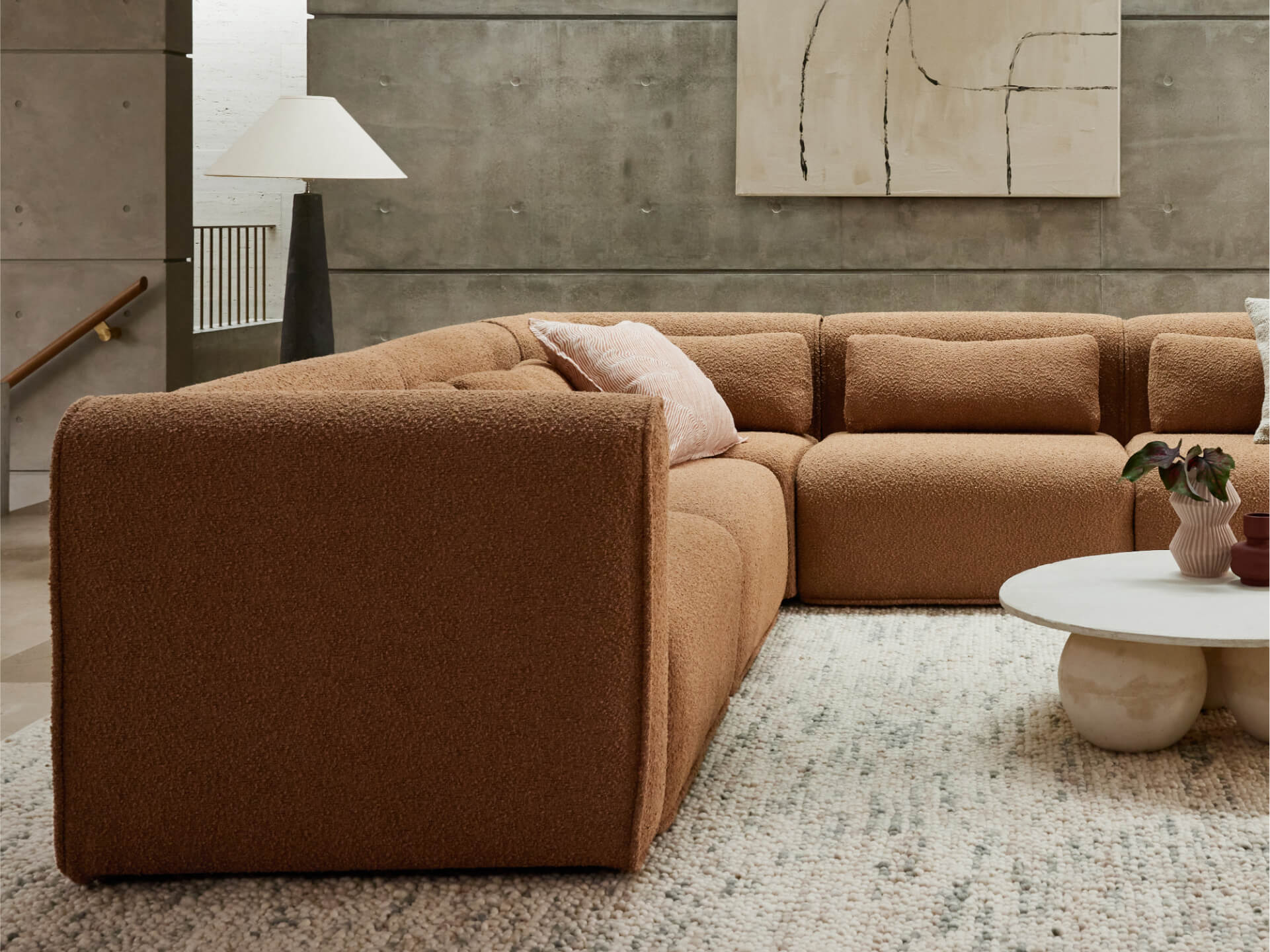 Luxurious sectional sofa in rich terracotta boucle fabric, featuring plush cushions and deep seats. Set on a textured cream rug in a modern living space.
