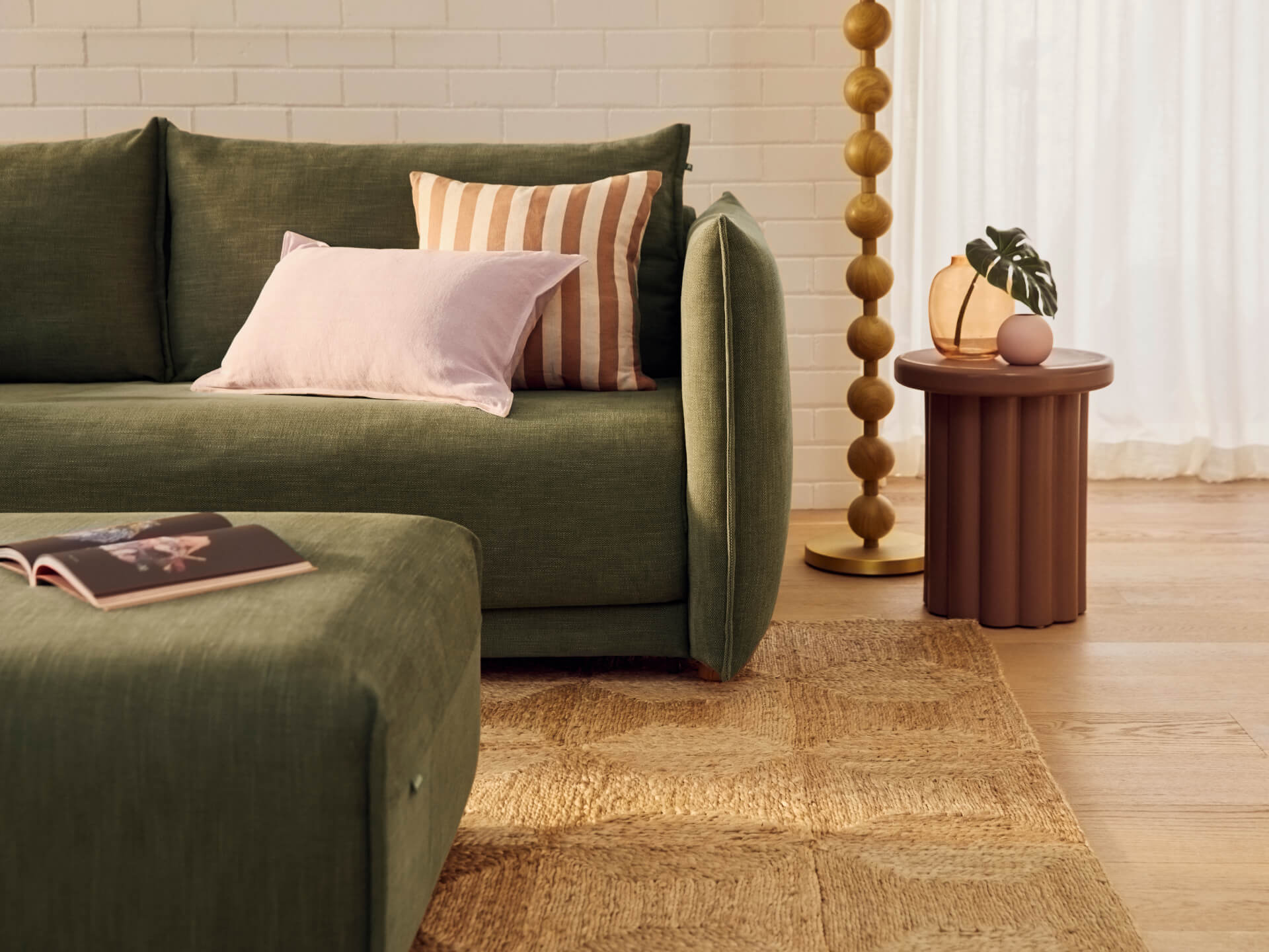 Luxurious olive-green linen sofa with plush cushions, wooden side table, and natural woven rug in a contemporary living room with warm wood flooring.