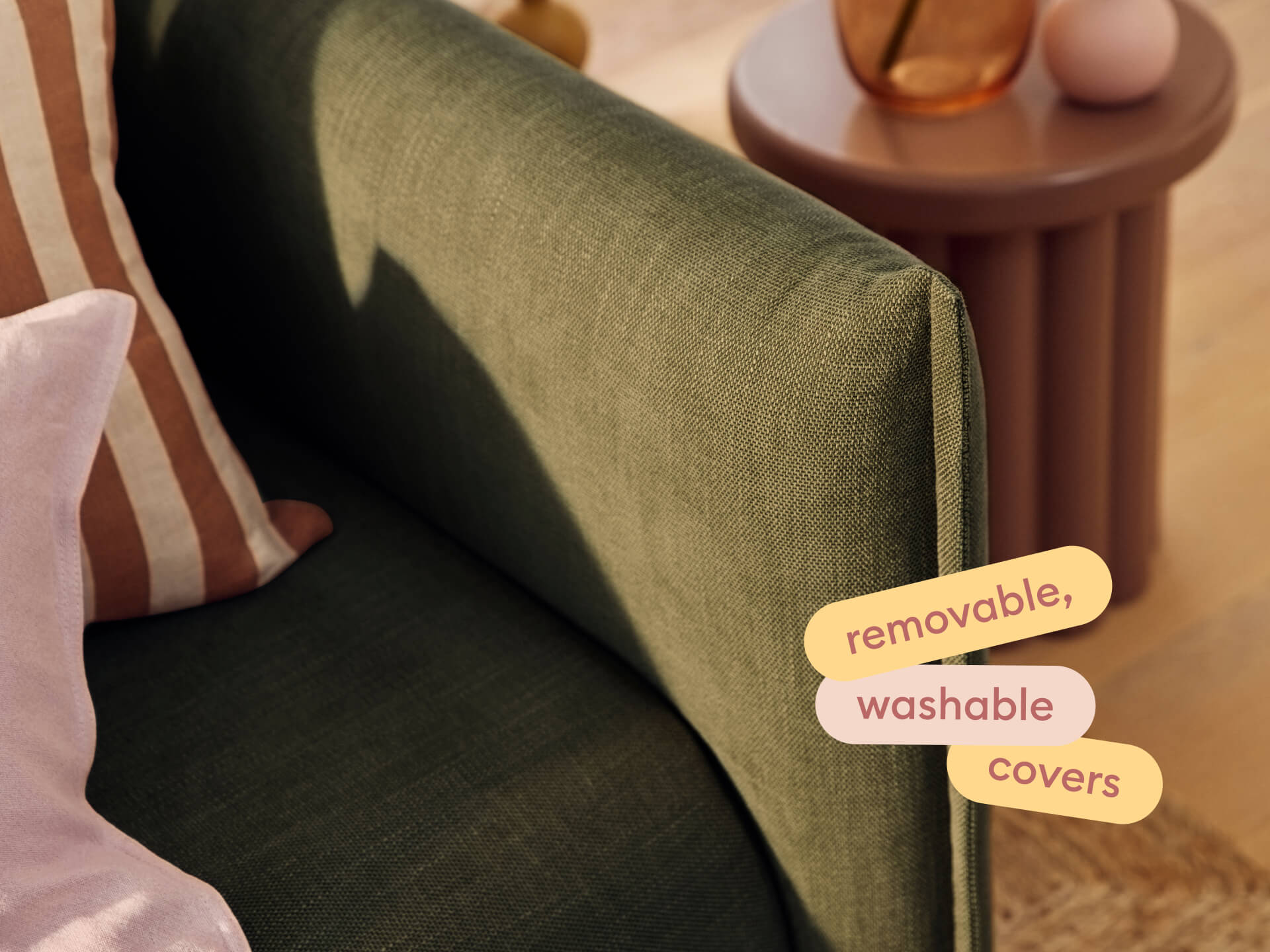 Luxurious green fabric sofa with removable, washable covers. Features elegant stitching and plush cushions. Paired with a round, mauve side table.