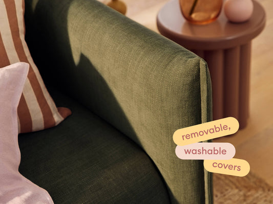 Luxurious green fabric sofa with removable, washable covers. Features elegant stitching and plush cushions. Paired with a round, mauve side table.