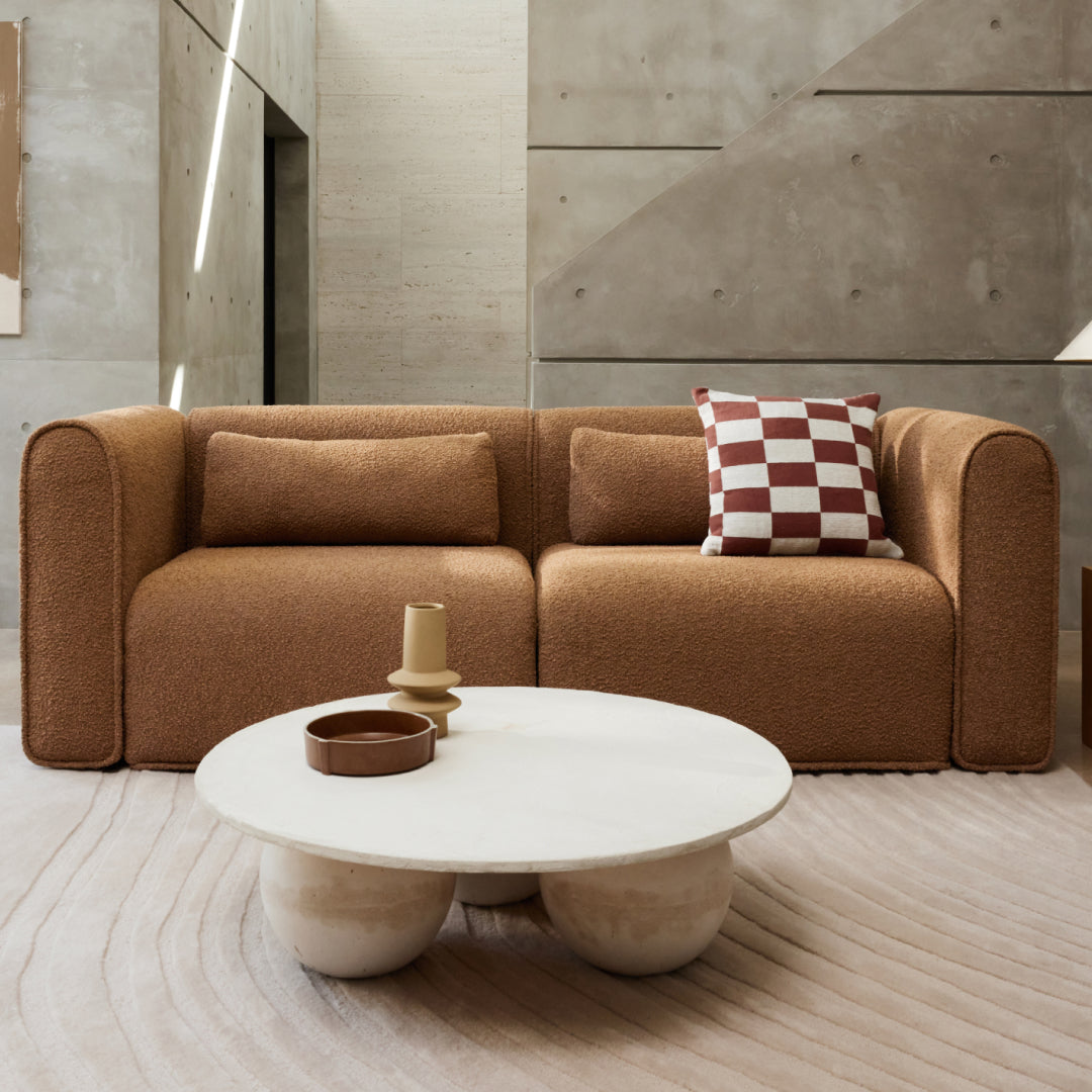 Luxurious modern sofa in textured brown boucle fabric with rounded arms, paired with a white circular coffee table. Set in an elegant, minimalist interior.