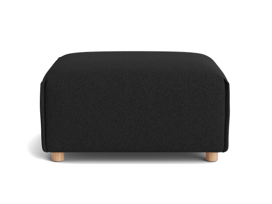 A square, black upholstered ottoman with light wooden legs, set against a black background.