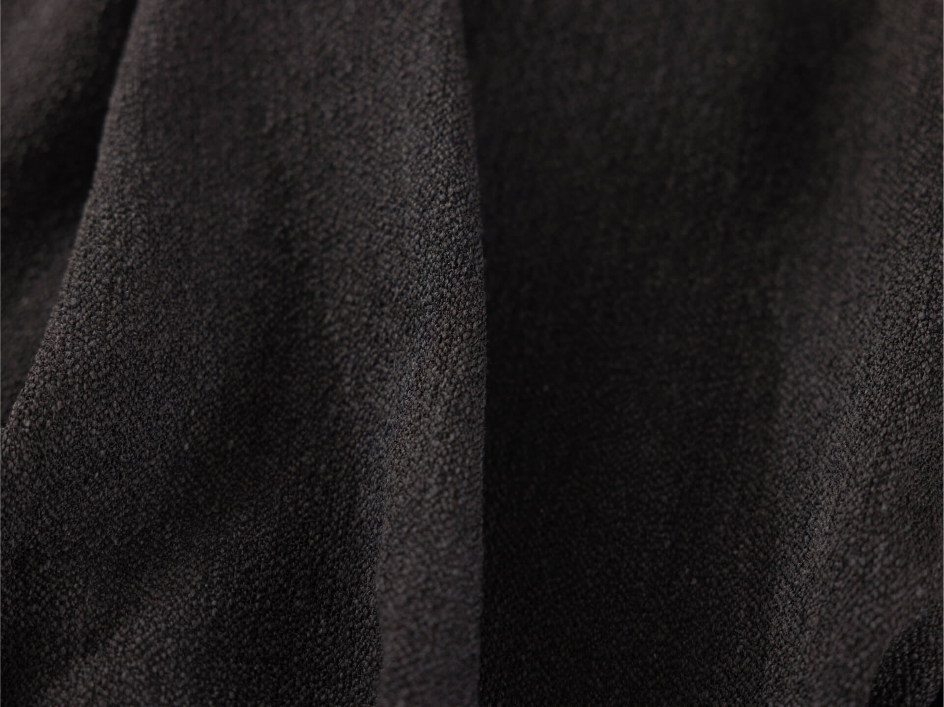 A close-up of soft, textured black fabric with a smooth, slightly shiny surface and subtle variations in light.