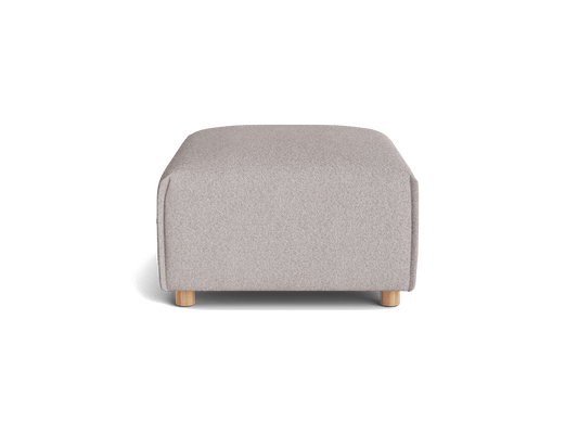 A light grey ottoman with rounded corners sits on natural wood legs, featuring a textured fabric surface.
