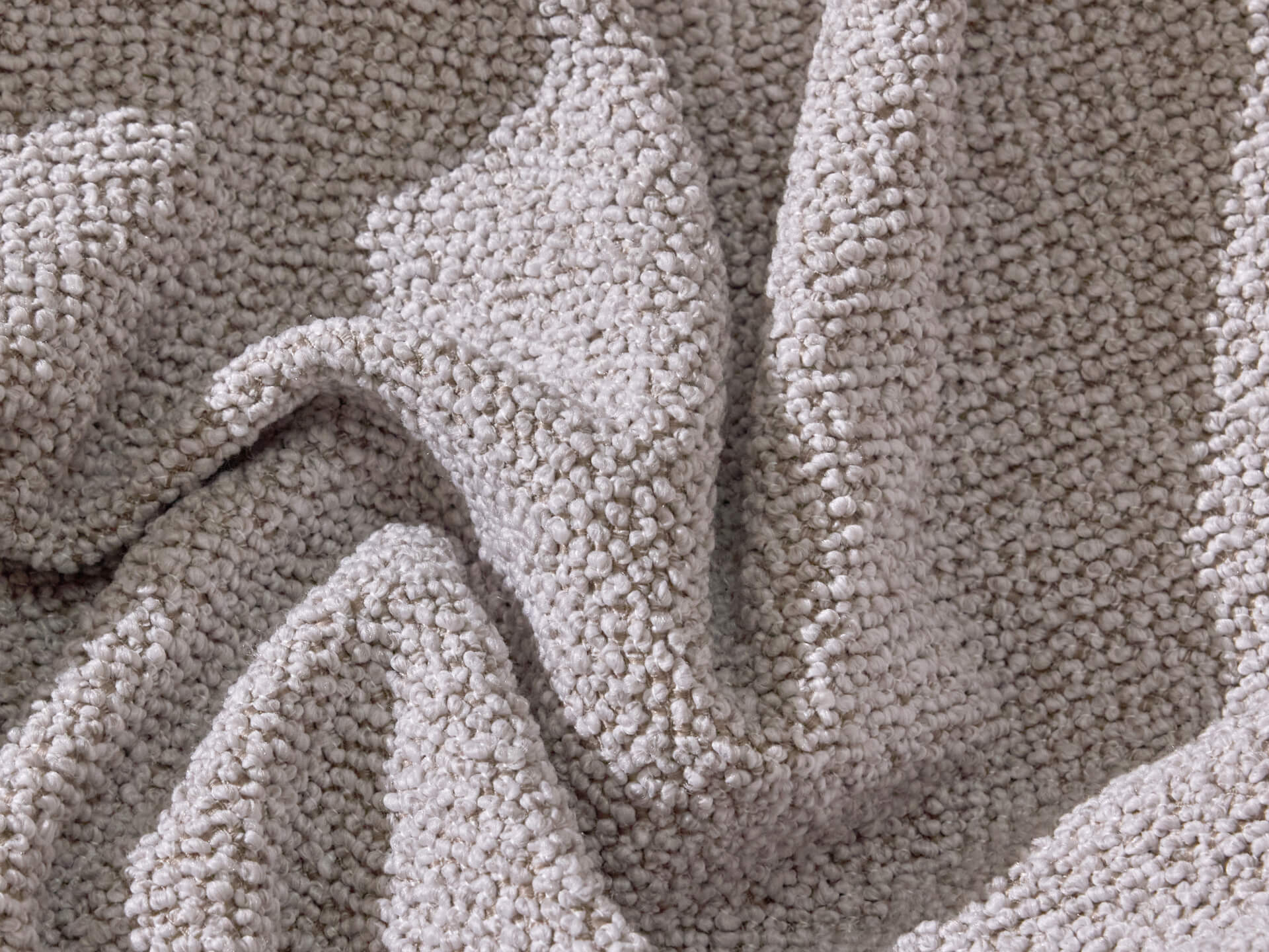 A close-up of textured, light grey fabric with a soft, cozy appearance, featuring intricate, looped patterns.