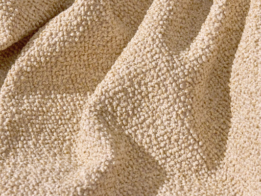 A close-up of textured beige fabric, featuring a soft, woven surface with small, raised fibers creating a cozy look.