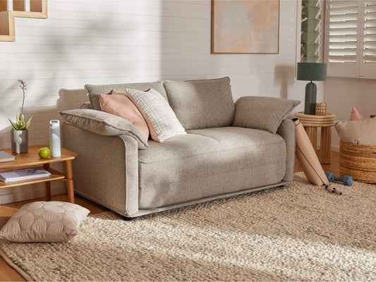 A light grey sofa with pink and textured pillows, beside a wooden table. A beige rug and wicker basket add warmth to the room.