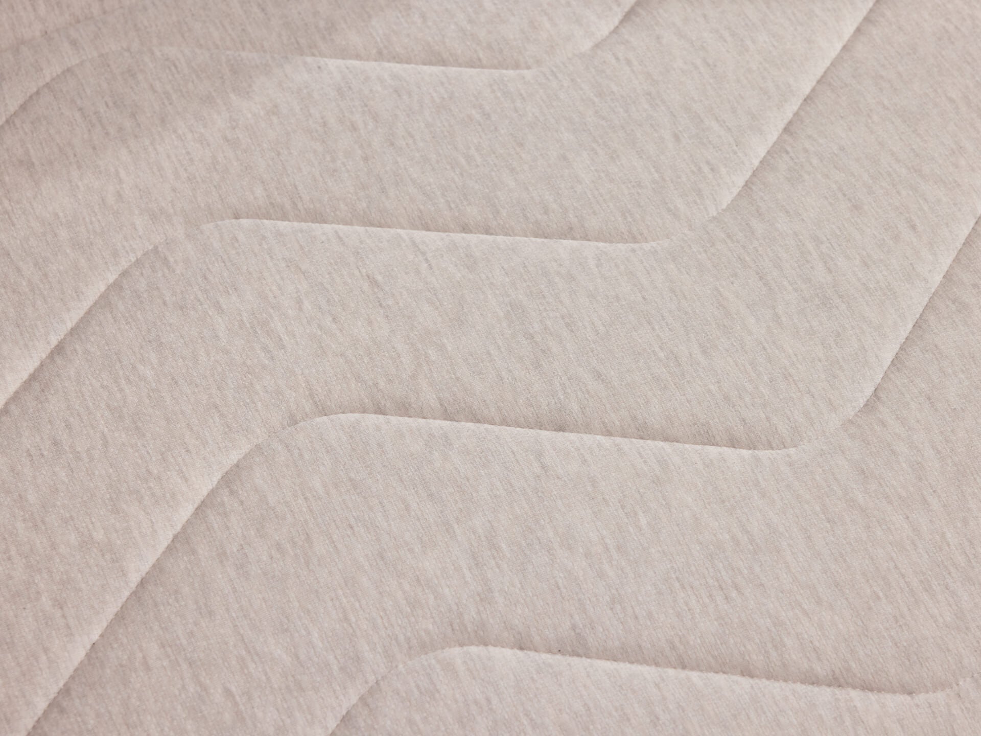 A close-up of beige fabric with a wavy quilted pattern, featuring subtle texture variations in light and shadow.