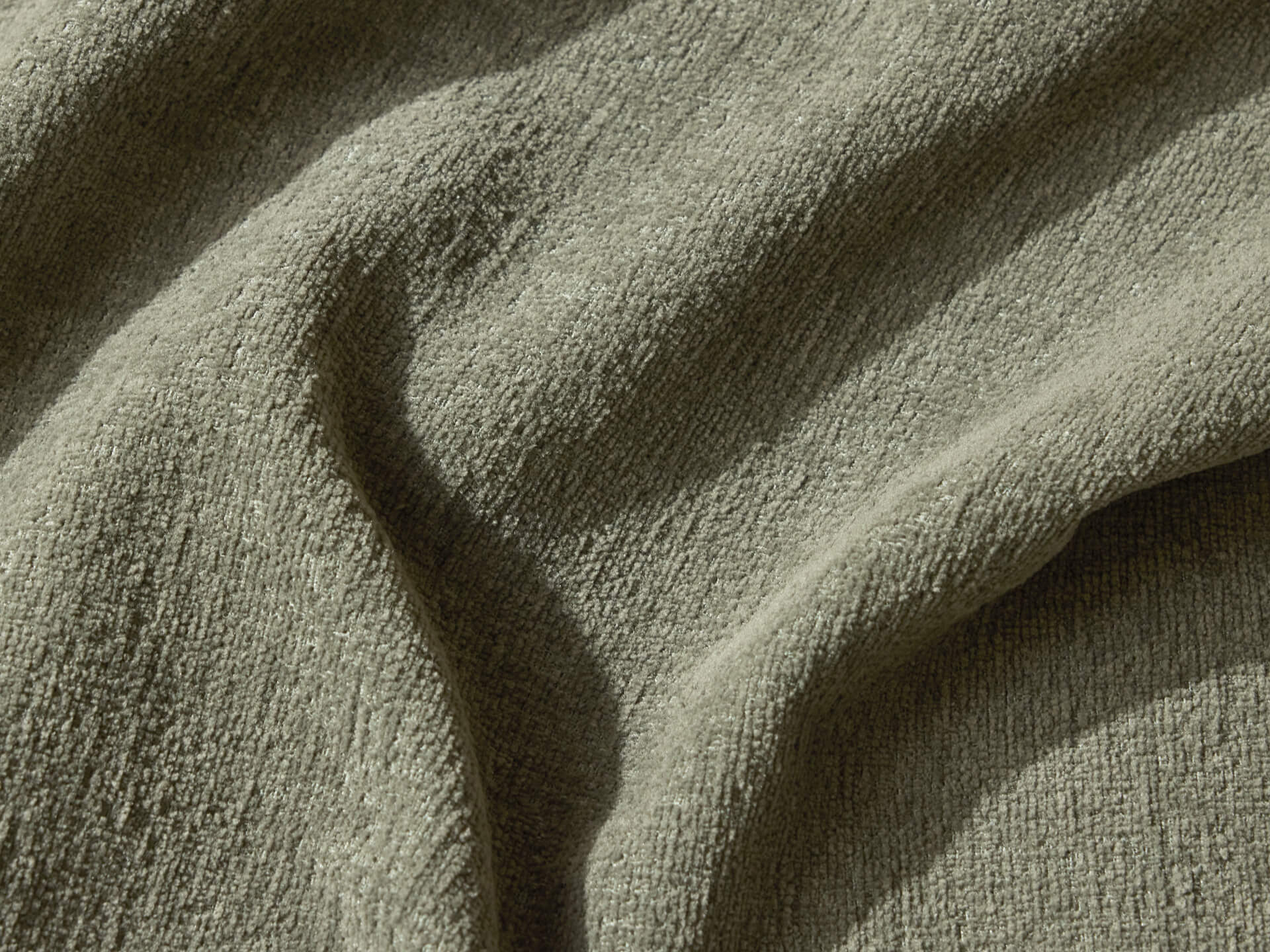 A close-up of textured fabric in a muted olive green color, featuring soft, wave-like folds and a plush appearance.