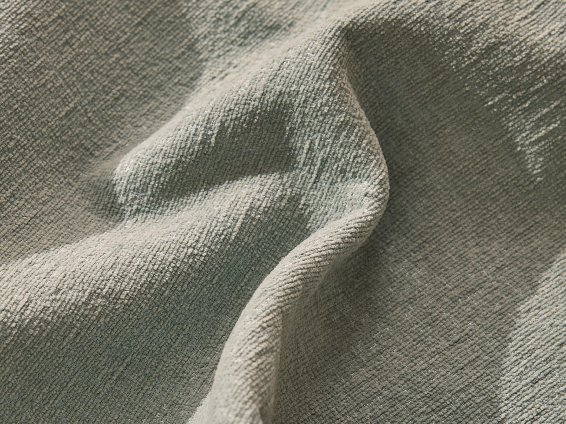 Close-up of textured fabric in a soft, muted mint green, with gentle folds and shadows highlighting its weave.