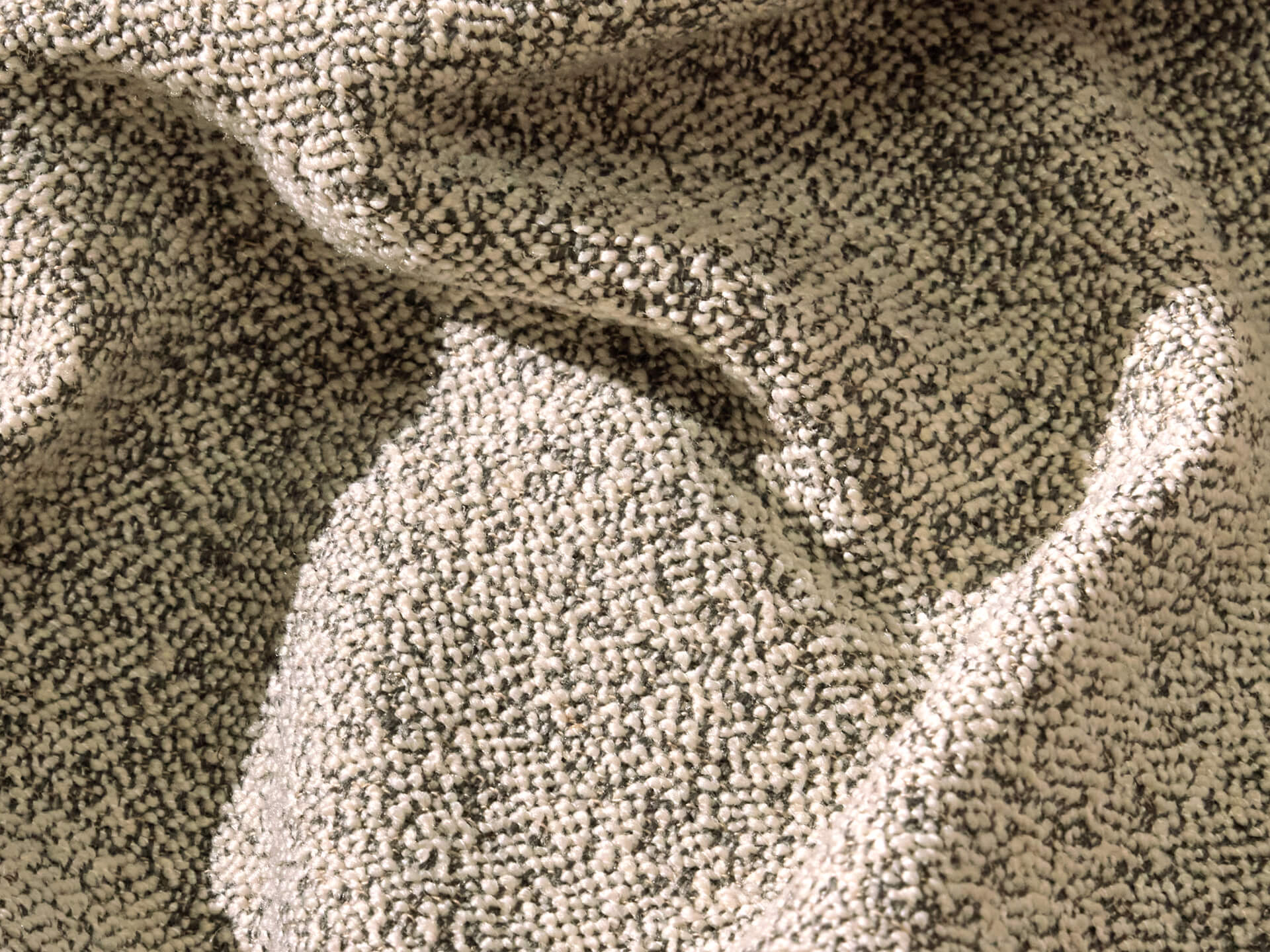 A close-up of a textured fabric with a light beige base and dark grey speckles, creating a rich, intricate pattern.