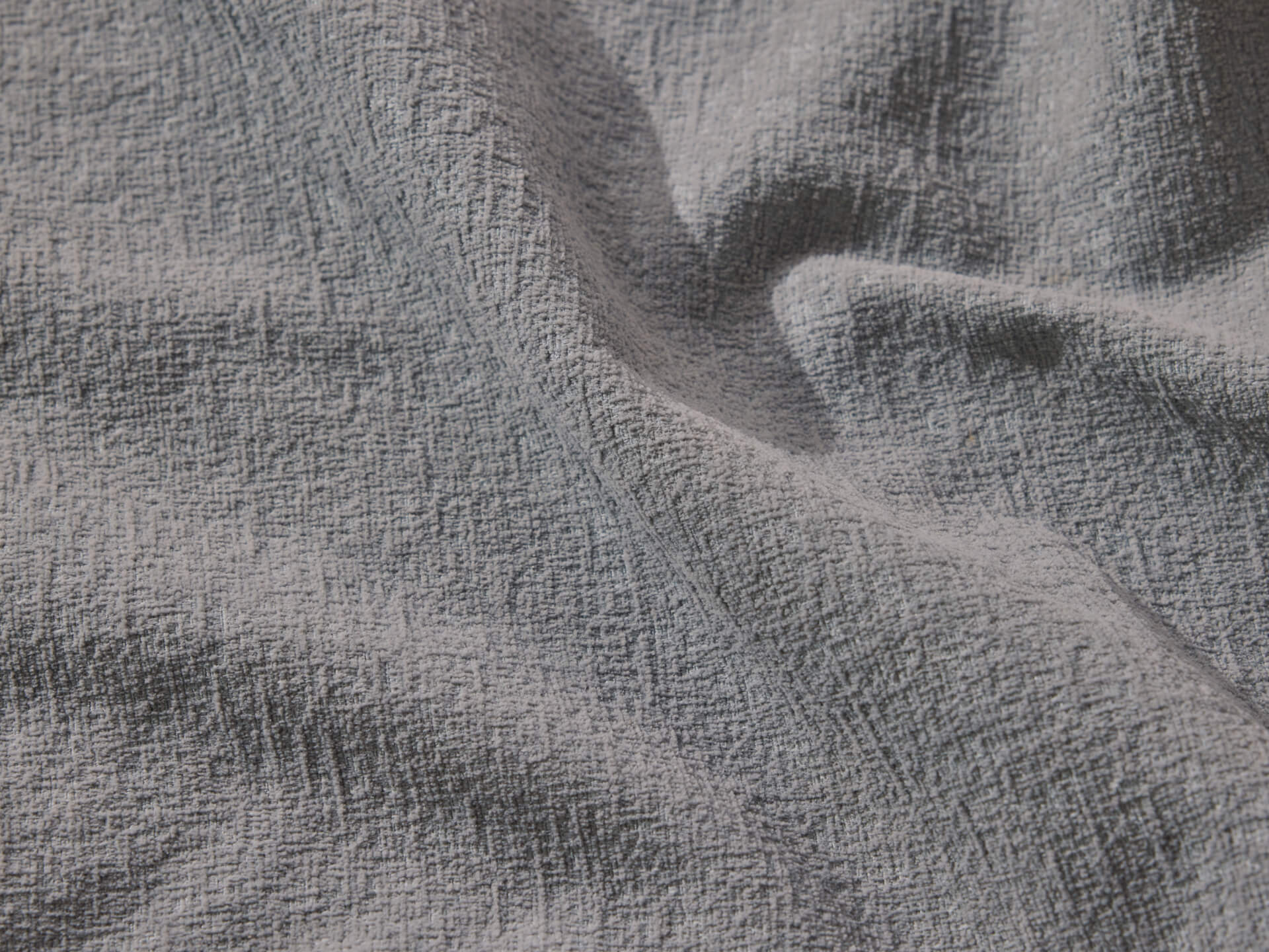 A close-up of textured fabric in a soft, muted light blue hue, displaying gentle ripples and an intricate woven pattern.