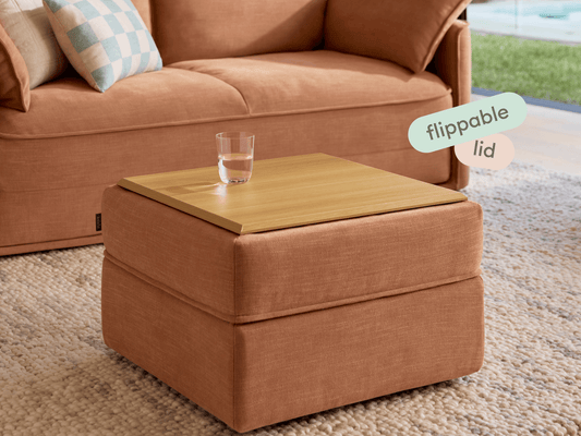 Modern square ottoman in rich terracotta fabric featuring a flippable timber lid. Set on a textured cream rug beside a plush sofa, offering versatile elegance.