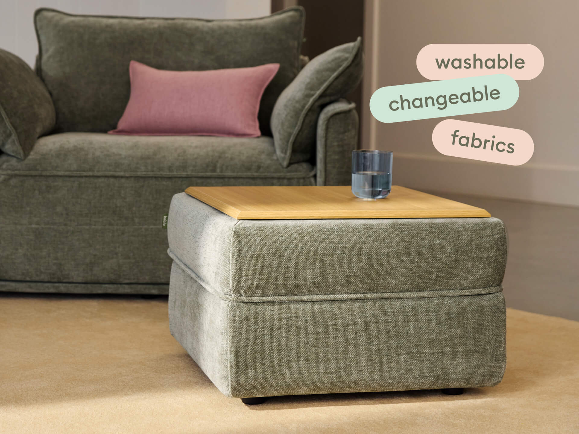 Elegant ottoman with green washable fabric and sleek wood top, paired with a matching sofa featuring a pink accent cushion, set on a beige carpet.