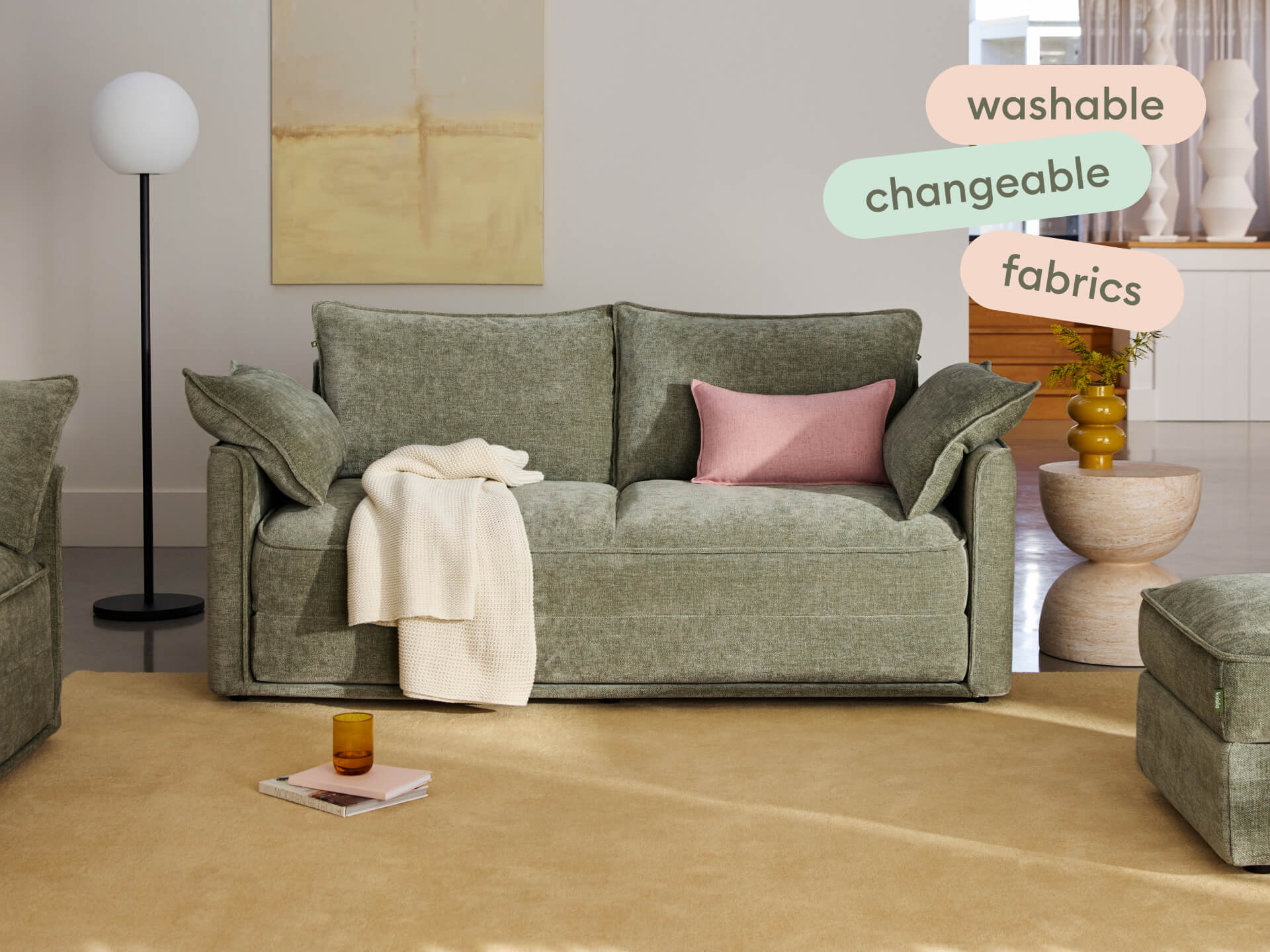 Elegant olive green sofa with plush, washable, and changeable fabric. Features soft cushions and sleek, boxy design. Set in a modern living room.