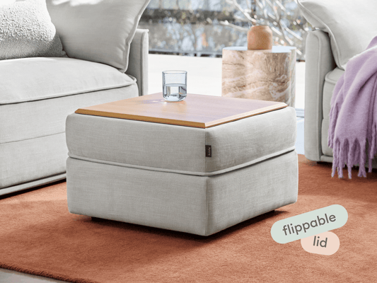 Luxurious ottoman with soft grey upholstery and a stylish oak wood flippable lid, placed on an elegant terracotta rug in a contemporary living room.