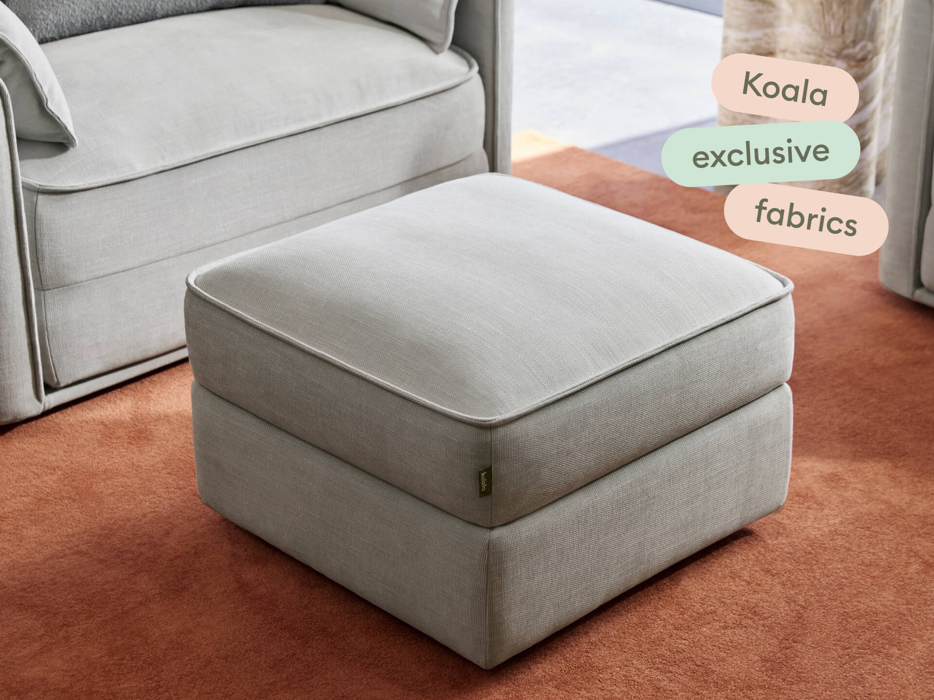 Luxurious grey fabric ottoman with a plush cushion top, set on a warm terracotta rug. Perfect for contemporary living spaces, enhancing comfort and style.