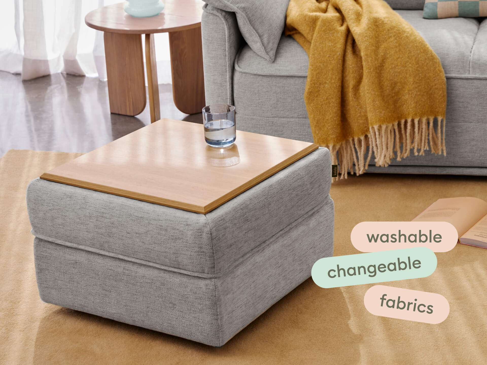Modern ottoman with grey upholstered fabric, light wooden top, and square design. Versatile, washable covers; ideal for contemporary living areas.