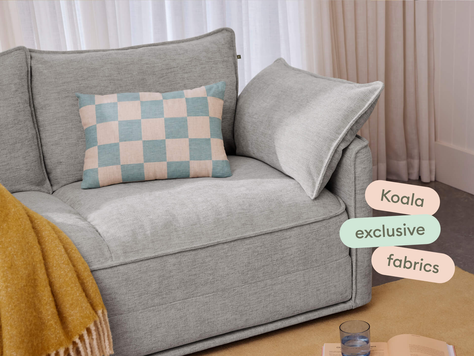 Modern grey fabric sofa with plush cushions, featuring exclusive materials, accented by a pastel checkered pillow. Set in an elegant, light-filled room.