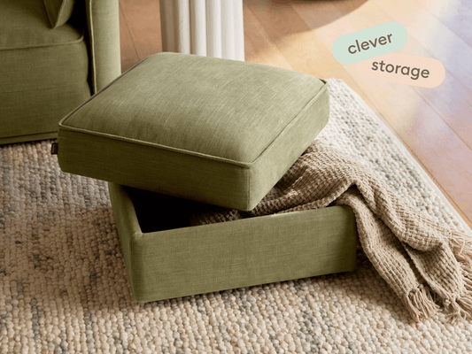 Olive green upholstered ottoman with removable top revealing hidden storage, set on textured beige rug in a chic living room with natural light.