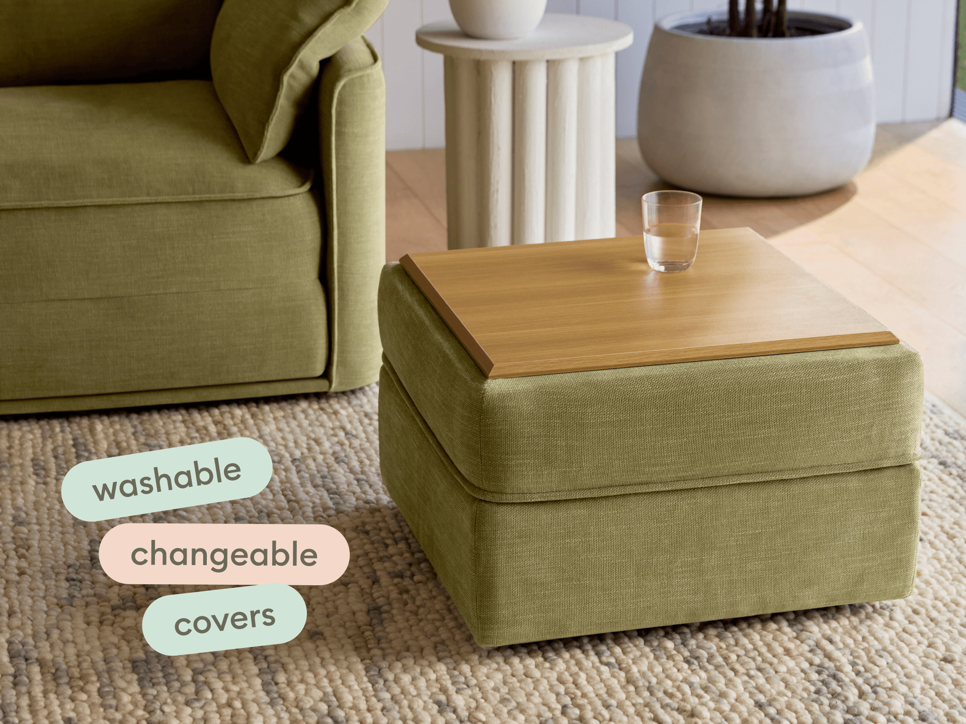 Olive green ottoman with a smooth timber top, featuring washable, interchangeable covers. Set on a textured rug beside a stylish armchair and ceramic pot.