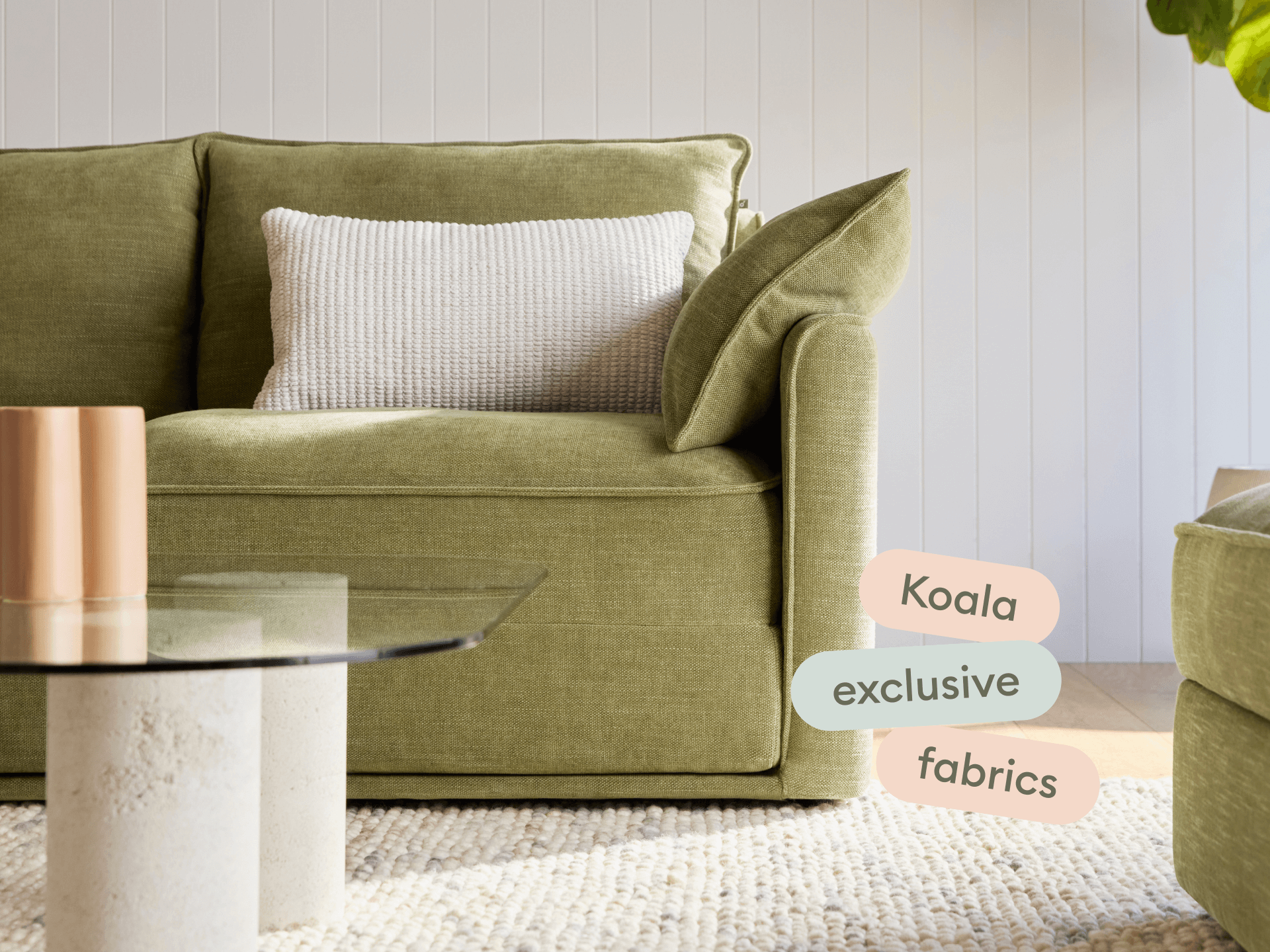 Luxurious olive-green fabric sofa with clean lines and plush cushioning, set on a woven rug. Features a glass coffee table in a serene, contemporary living room.