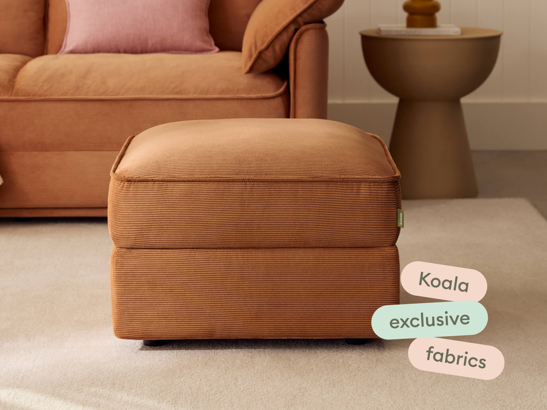 Luxurious corduroy ottoman in rich burnt sienna; plush upholstery, timeless design. Set in an elegant living room with warm neutrals and modern accents.