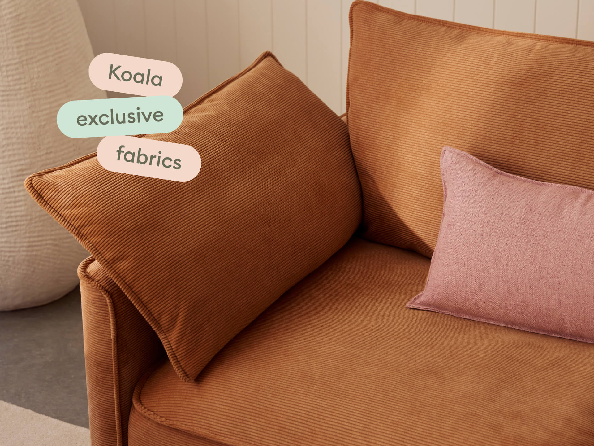 Elegant terracotta corduroy sofa with plush cushions, featuring a chic blush accent pillow. Set against a warm neutral backdrop for a sophisticated lounge.