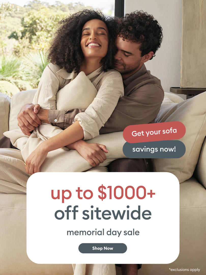 Smiling couple embracing on cream Koala sofa above 'up to $1000+ off sitewide memorial day sale' banner