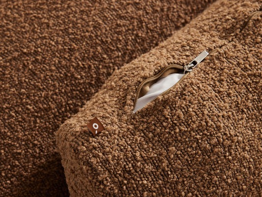 Brown boucle cushion with a metallic zipper and concealed pocket, featuring a soft, textured finish. Perfect for contemporary living room settings.