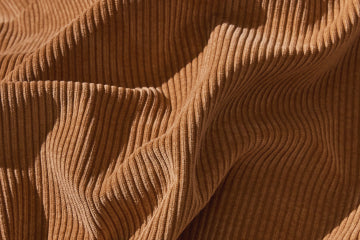 Close-up of luxurious tan corduroy fabric, showcasing its soft texture and fine ribbed detailing, perfect for high-end upholstery applications.