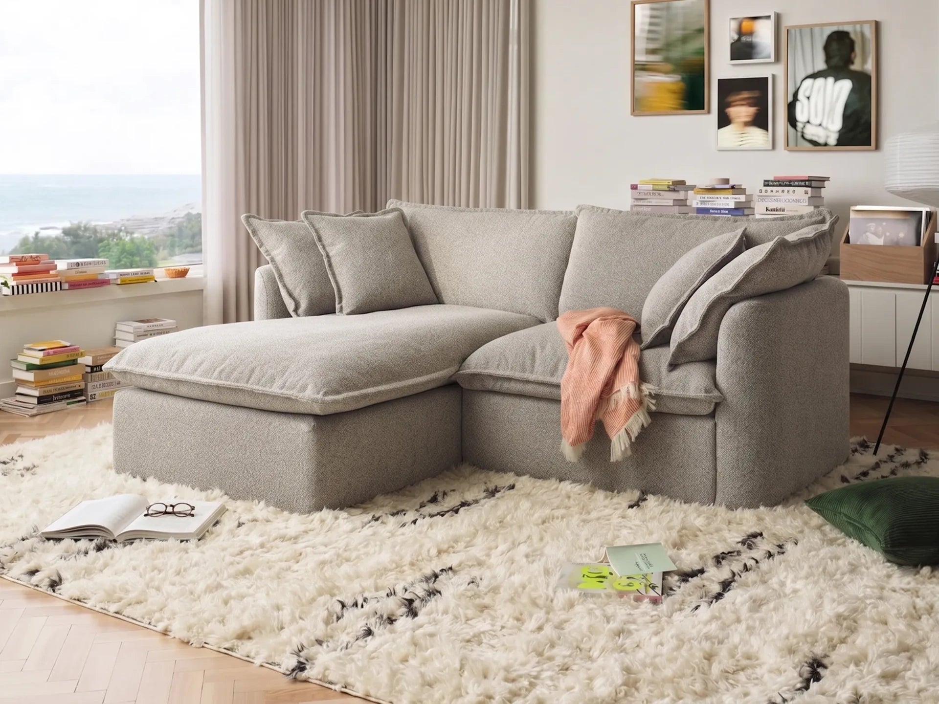 Gray sectional sofa in a living room with a white rug and books on a shelf.