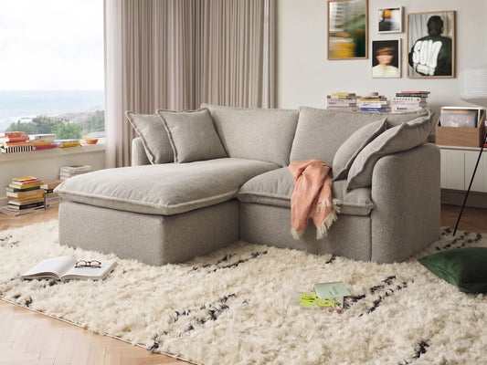 Gray sectional sofa in a living room with a white rug and books on a shelf.