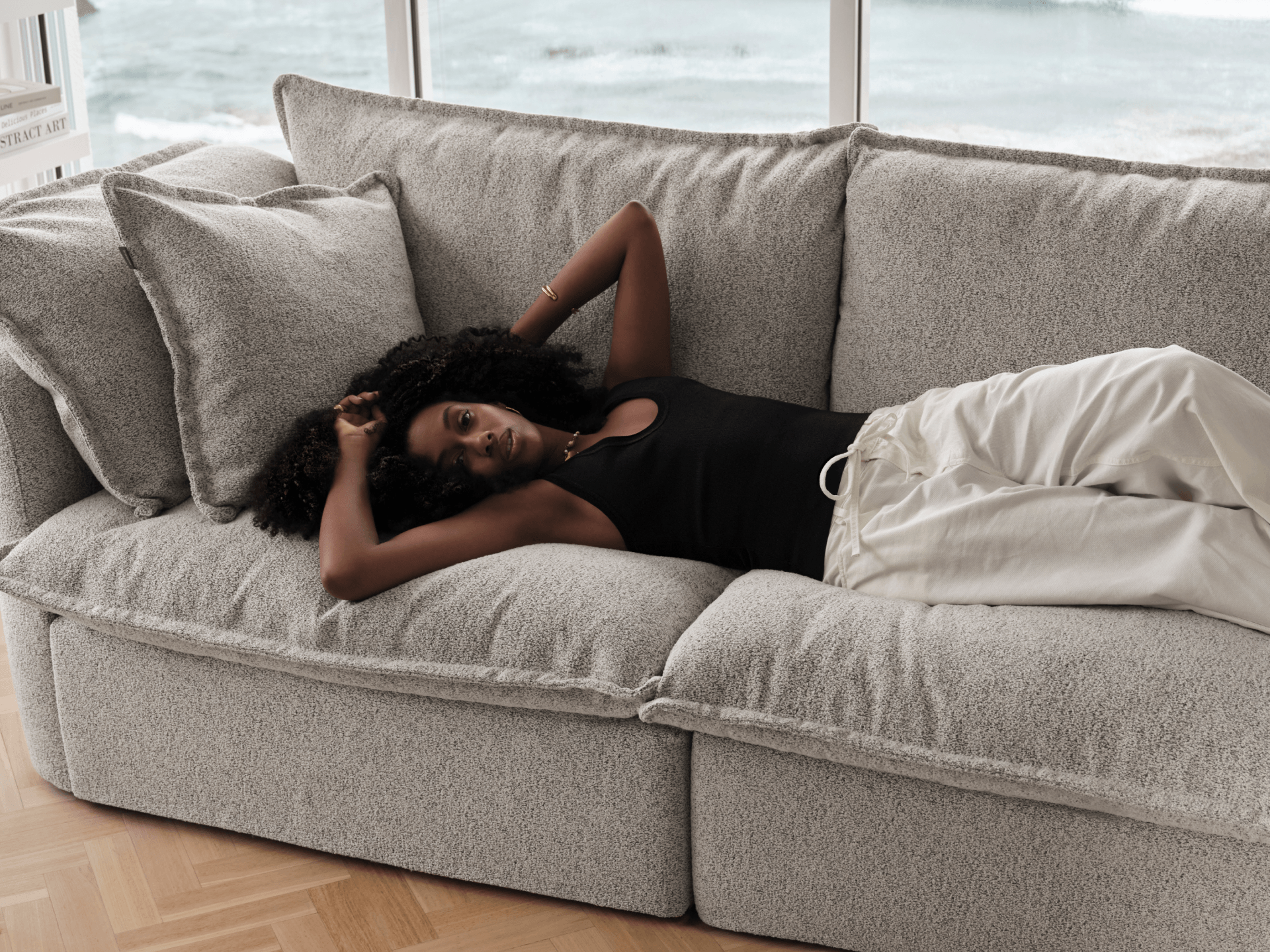 Koala Tamarama 2-section modular sofa in Aussie Latte, with model, brown knit cushion and bookshelves backdrop