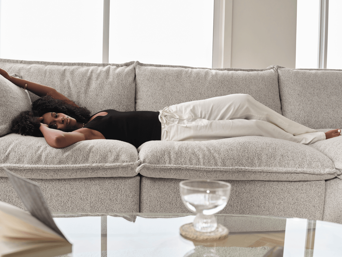 Koala Tamarama 4-section modular sofa in Aussie Latte, with model, brown knit cushion and bookshelves backdrop