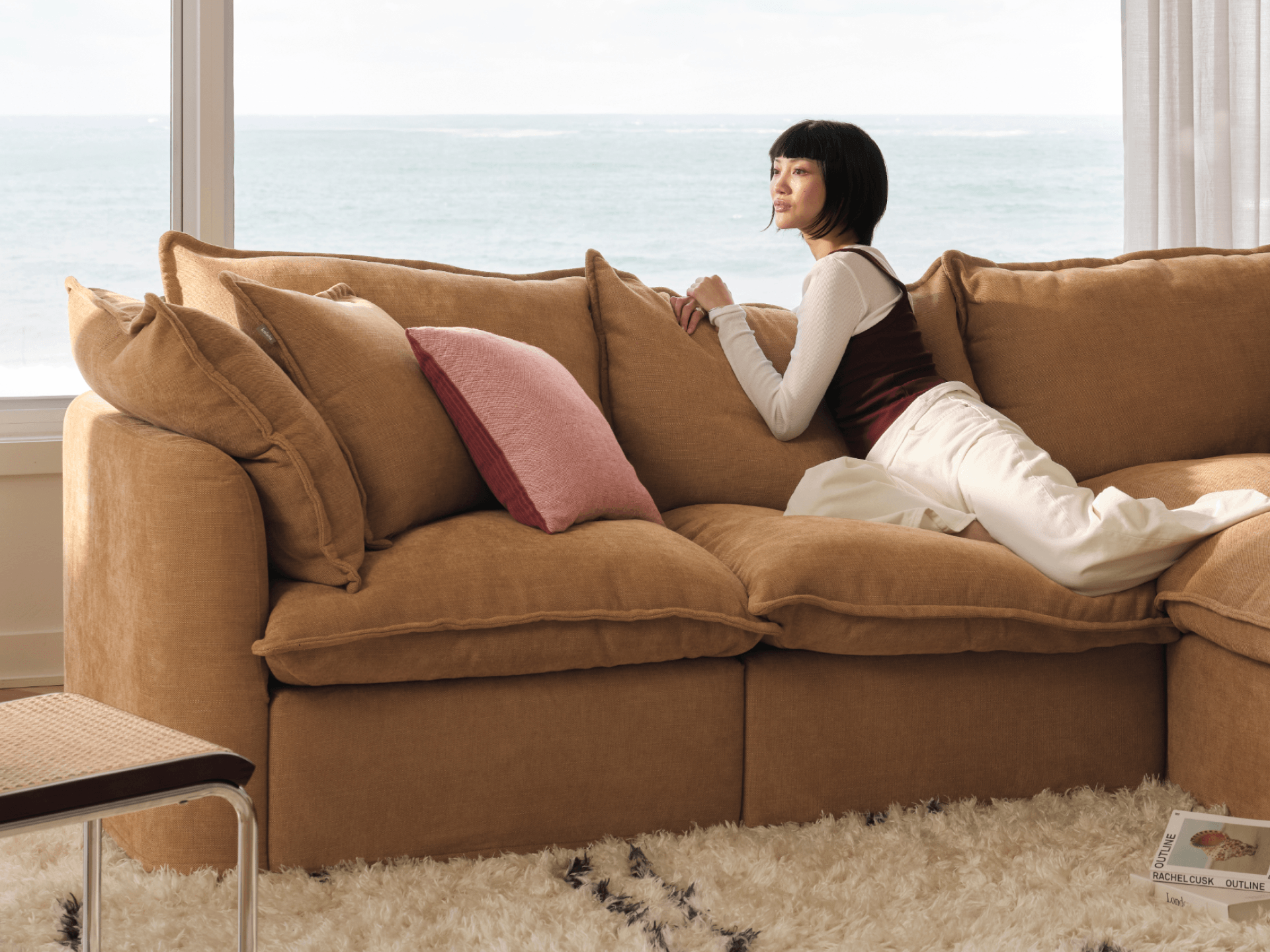 Koala Tamarama 4-section L-shape sectional in Bronzed Aussie, with model, brown knit cushion and bookshelves backdrop