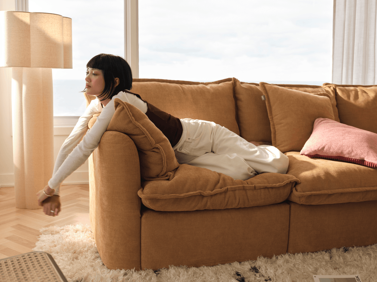 Koala Tamarama 4-section modular sofa in Bronzed Aussie, with model, brown knit cushion and bookshelves backdrop