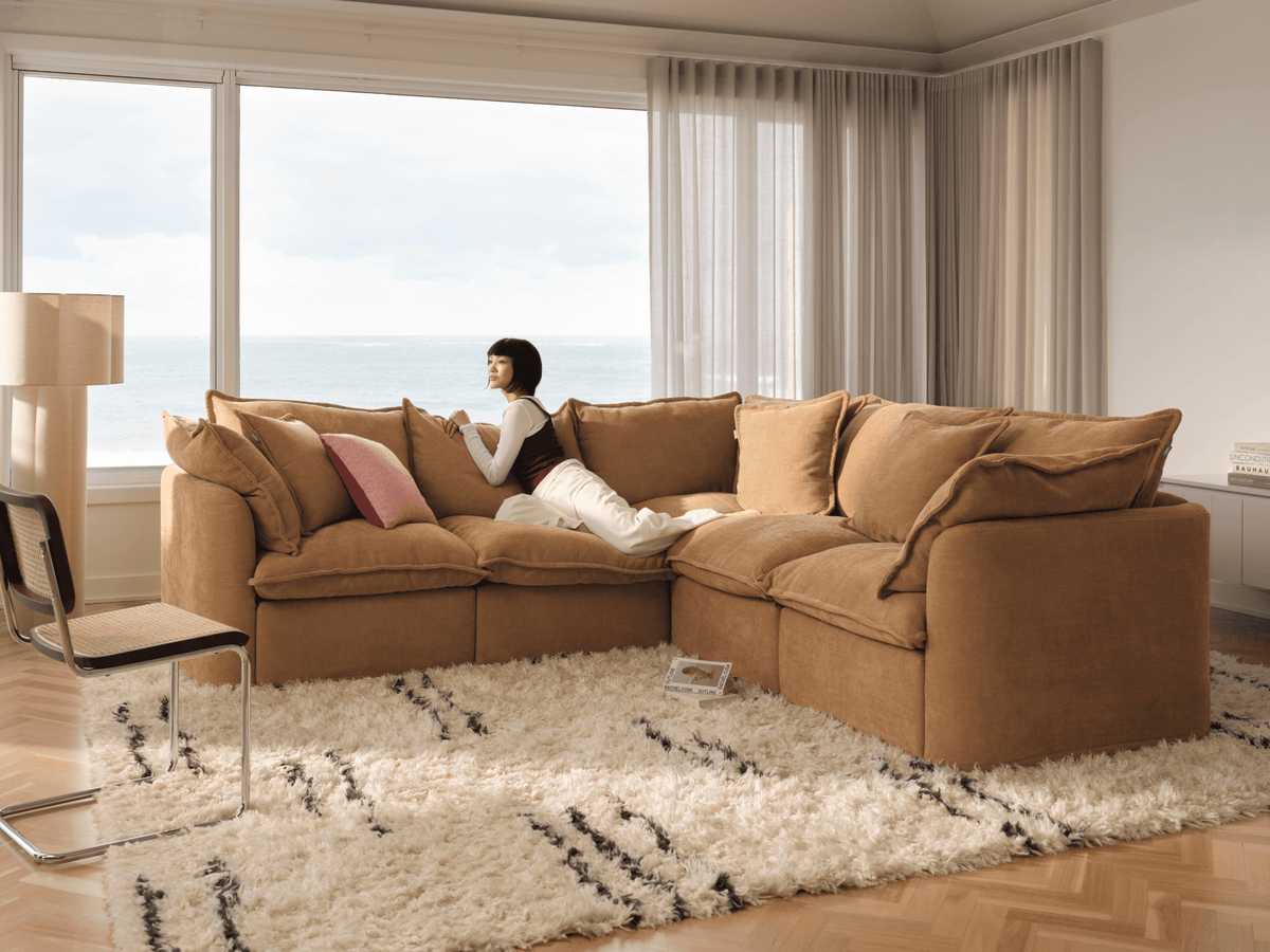 Koala Tamarama 5-section L-shape sectional in Bronzed Aussie, with model, brown knit cushion and bookshelves backdrop