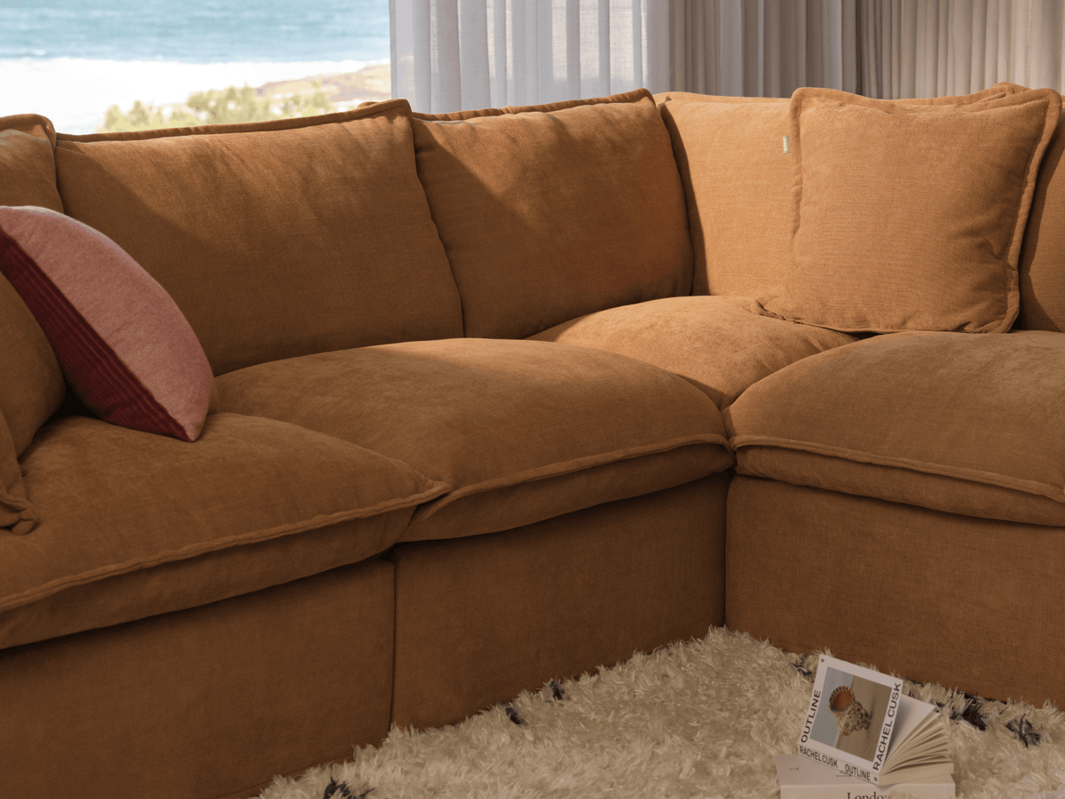 Koala Tamarama 6-section U-shape sectional in Bronzed Aussie, with model, brown knit cushion and bookshelves backdrop