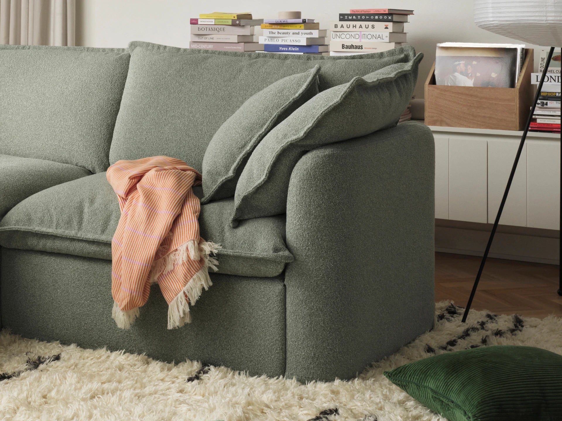 Green sofa with a pink blanket on a white rug in a living room setting.