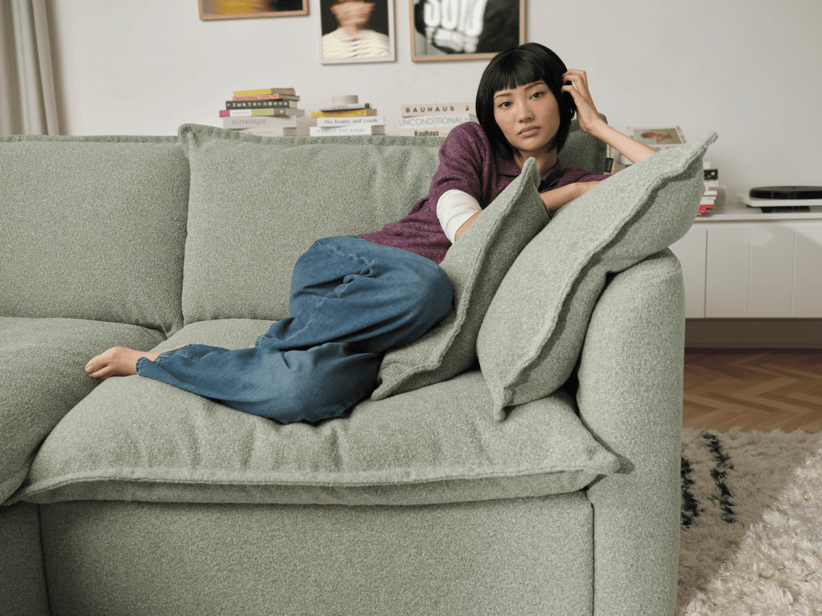 Koala Tamarama 4-section L-shape sectional in Frosty Grass, with model, brown knit cushion and bookshelves backdrop