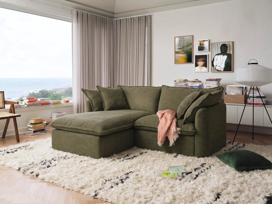 Green sectional sofa in a living room with a white rug and large window.